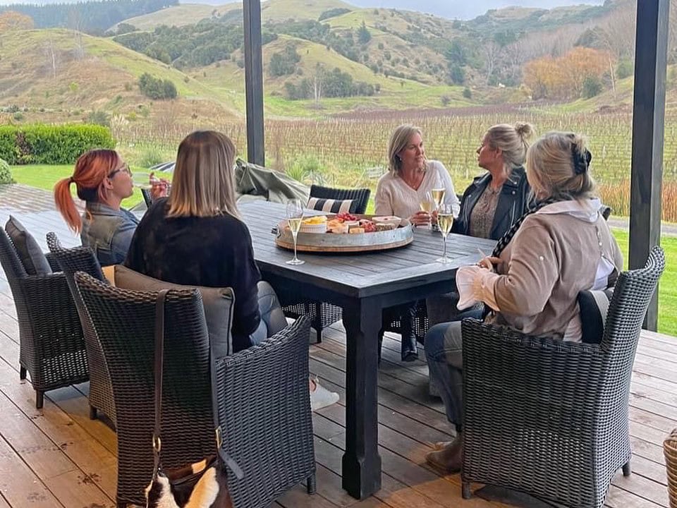 A group of woman sitting at a table enjoying a glass of wine outside the Vineyard Villa at Kiwiesque